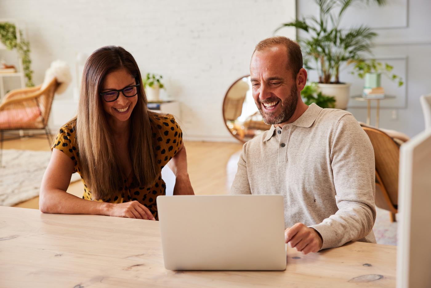 A couple working through business listings together on a laptop at their kitchen table