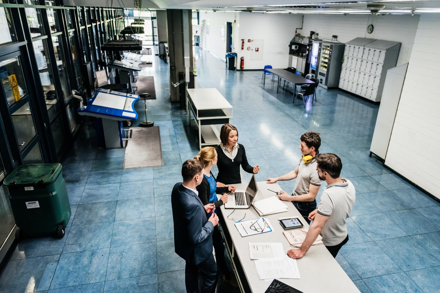 An operator and team gathered around a work table on a shop floor, reviewing plans together